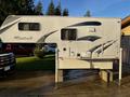 A 2023 Westland 80W 8 Foot truck camper with a white exterior featuring blue and gray abstract designs and mounted on supports