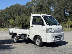 A white 2009 Daihatsu Hijet mini truck with a flatbed and a single cab parked on a gravel surface