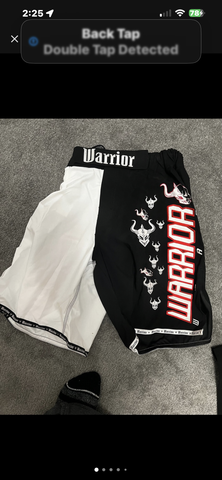 Black and white MMA shorts featuring the word "Warrior" in bold red letters and graphic designs of a bull on the fabric