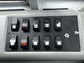 A control panel with multiple black switches and buttons on a gray surface featuring various symbols and labels for different functions