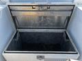 A silver metal storage box with diamond plate texture and a hinged lid is open, revealing an empty interior with some dark material at the bottom