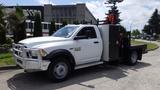 A white 2014 RAM 5500 pickup truck with a flatbed and tool storage on the side is parked prominently in the foreground