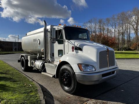 A 2013 Kenworth T370 truck with a large silver tank and orange lights on the roof parked on a road