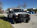 A white 2008 Ford F-450 SD with a flatbed and front grille guard parked on a street