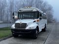 A white 2016 International 4200 bus with a large windshield and multiple amber lights on the roof parked on a street