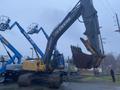 A 2014 John Deere 350G excavator with a large bucket attachment stands prominently in the foreground