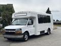 A 2020 Chevrolet Express shuttle bus with a white exterior and large tinted windows, designed for passenger transport