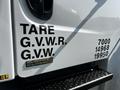 A white 2004 Freightliner M2 truck with visible labels for tare weight and gross vehicle weight ratings on the side