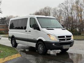 A white 2008 Dodge Sprinter van with dark tinted windows and alloy wheels parked on a wet surface
