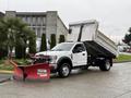 A white 2021 Ford F600 dump truck with an upraised bed and a red snow plow attached to the front