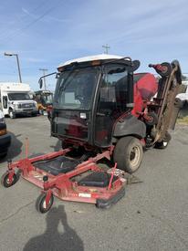 A 2013 Toro Grounds Master 5910 turf maintenance vehicle with a cab and a front-mounted mowing deck is parked on a concrete surface