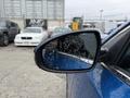 A close-up of the side mirror of a blue 2021 Kia Forte showing droplets of water on the surface