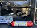 A red fire extinguisher is placed on the floor of a vehicle beside a seat mount mechanism