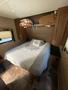 A neatly made bed with a gray and white quilt in a small, cozy camper interior featuring storage cabinets above the bed