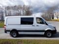 A 2016 Mercedes-Benz Sprinter van in white with black accents parked on a road showcasing its side profile and large cargo area