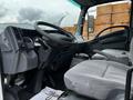 Interior view of a 2018 Isuzu NRR showcasing the driver's seat dashboard and controls with a gray seating fabric and a simple layout for visibility and accessibility