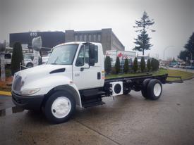 A white 2006 International 4300 truck with a flatbed and no cargo parked on a concrete surface