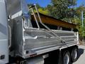 A silver 2005 Volvo VND 122 dump truck with a large yellow dump bed and hydraulic lift system on the rear side