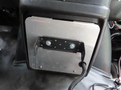 A metal mounting plate attached to a vehicle's dashboard with visible screws and a coiled wire extending from it