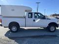 A white 2016 Ford F-250 SD with a camper shell on the bed is shown in profile view