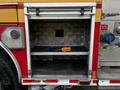 A compartment of a fire truck displaying an empty shelf with a black hose coiled and an orange tool positioned on the floor