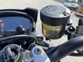 A close-up view of the handlebar controls of a 2018 Triumph Street Triple RS featuring a clear brake fluid reservoir and various switches and dials