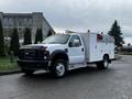 A 2009 Ford F-550 utility truck with a white body and black front, equipped with service compartments and light bars on top