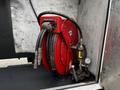 A red hose reel with two black hoses attached and a pressure gauge mounted on a metallic surface