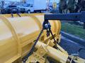 A yellow snowplow attachment with a curved blade and a chain hoist mechanism is shown in the foreground