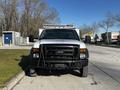 A 2008 Ford F-450 Super Duty truck with a white exterior and black grill parked on a street facing forward