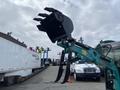 A 2024 AGT Industrial Green QH13R Mini Excavator with a black attachment in the foreground showcasing its hydraulic arm and gripping claws