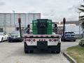 A 2013 Kenworth T370 flatbed truck with a green container secured on the back and rear-facing red safety lights
