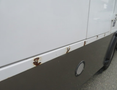 A white 2020 Chevrolet Express van with noticeable rust spots along the lower edge of its side panel