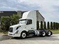 A 2012 Volvo VNL truck in white with a sleek design and a tall cab is parked with visible wheels and a chassis ready for cargo transport
