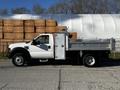 A 2008 Ford F-450 SD with a white cab and a silver flatbed is parked on a concrete surface the truck has a tool compartment on the side