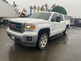 A white 2015 GMC Sierra 1500 pickup truck with a silver grille and large tires parked on a wet surface