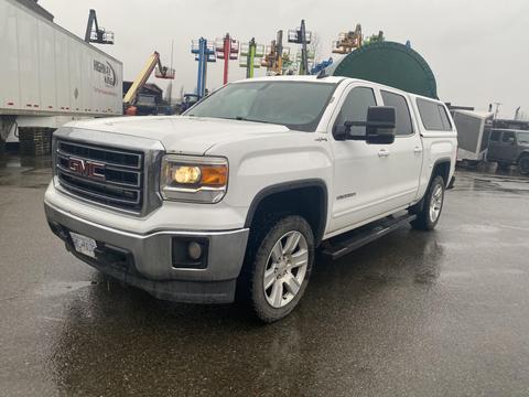 A white 2015 GMC Sierra 1500 pickup truck with a silver grille and large tires parked on a wet surface