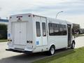 A white 2010 Ford Econoline shuttle bus with large windows and a wheelchair access sign on the side is parked on the street