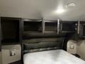 Interior of a 2021 Grand Design Recreation 311BHS featuring a large bed with a patterned mattress and overhead storage cabinets without doors above it
