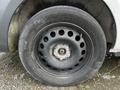 A close-up view of a black steel wheel with several holes and a worn tire mounted on it