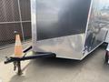 A metallic 2020 Stealth Enterprises trailer with a diamond plate exterior and a black hitch attached to a wheel chock and an orange traffic cone placed on the ground