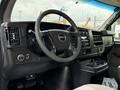 The interior of a 2015 GMC Savana features a steering wheel dashboard controls and gear shifter in a dark color scheme with a light fabric seat