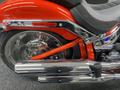 Close-up of a 2024 Harley Davidson Fat Boy showcasing its chrome exhaust pipes and red frame details with a black seat and visible brake elements