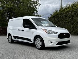A white 2019 Ford Transit Connect van is parked at an angle showcasing its front and side view with a smooth design and alloy wheels