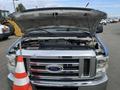 A blue 2009 Ford Econoline van with its hood raised revealing the engine compartment and a red and white striped traffic cone in front
