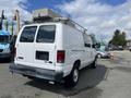 A white 2009 Ford Econoline van with a roof rack and no visible license plate is parked with its rear facing the viewer