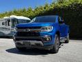 A blue 2021 Chevrolet Colorado is parked, showcasing its front view with a bold grille and sleek design, highlighting the vehicle's sporty appearance and modern features.