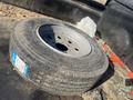 A worn tire with a silver rim lying on the ground, showing signs of use and dirt on the surface