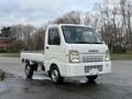 A white 2009 Suzuki Carry pickup truck parked with an open cargo bed and a compact design featuring a simple front grille and rounded headlights