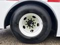 A close-up of a large tire on a white wheel with black lettering and bright green bolts securing the rim to the hub